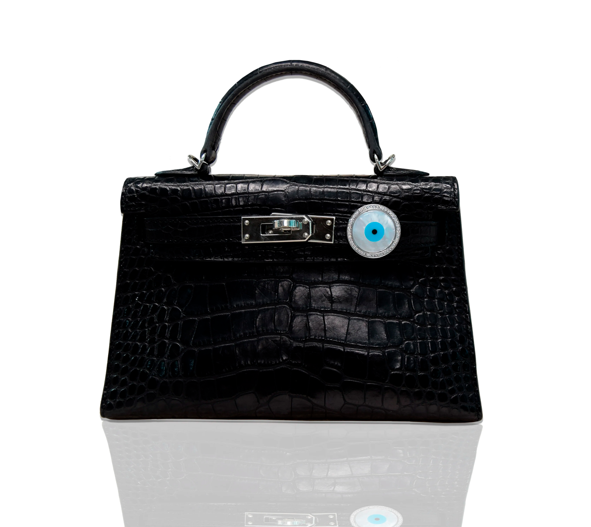 A luxury handbag with a black crocodile pattern and an 18kt gold, diamond, and mother of pearl evil eye design bijoux attached to it, collection-preview.