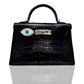 A black handbag with a marquise-shaped blue evil eye accessory affixed to it, set against a white background, collection-preview.