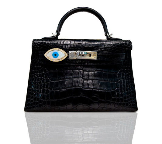 A black handbag with a marquise-shaped blue evil eye accessory affixed to it, set against a white background, collection-preview.