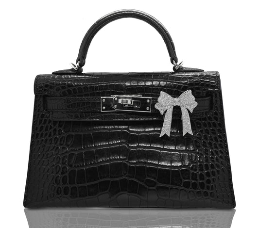 A black handbag with a crocodile pattern, featuring a silver bow custom attachment, collection-preview.