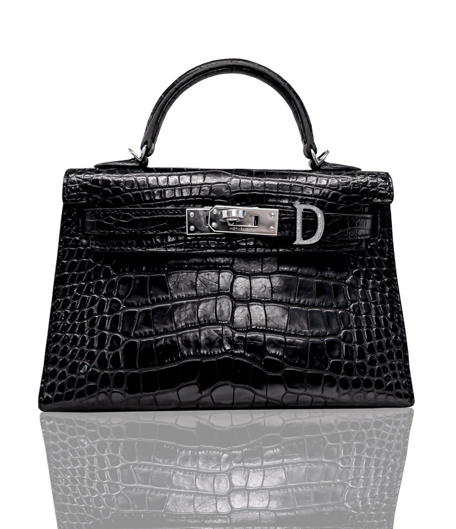A black handbag with a crocodile pattern and a metallic clasp, resembling a 'D' shaped hardware, typically seen on luxury leather handbags, collection-preview.