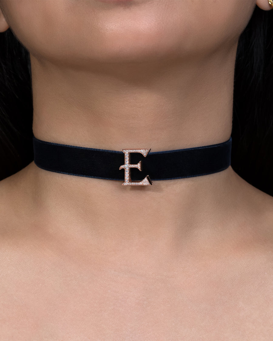 Navy blue velvet choker with a gold 'E' clasp on a person's neck.