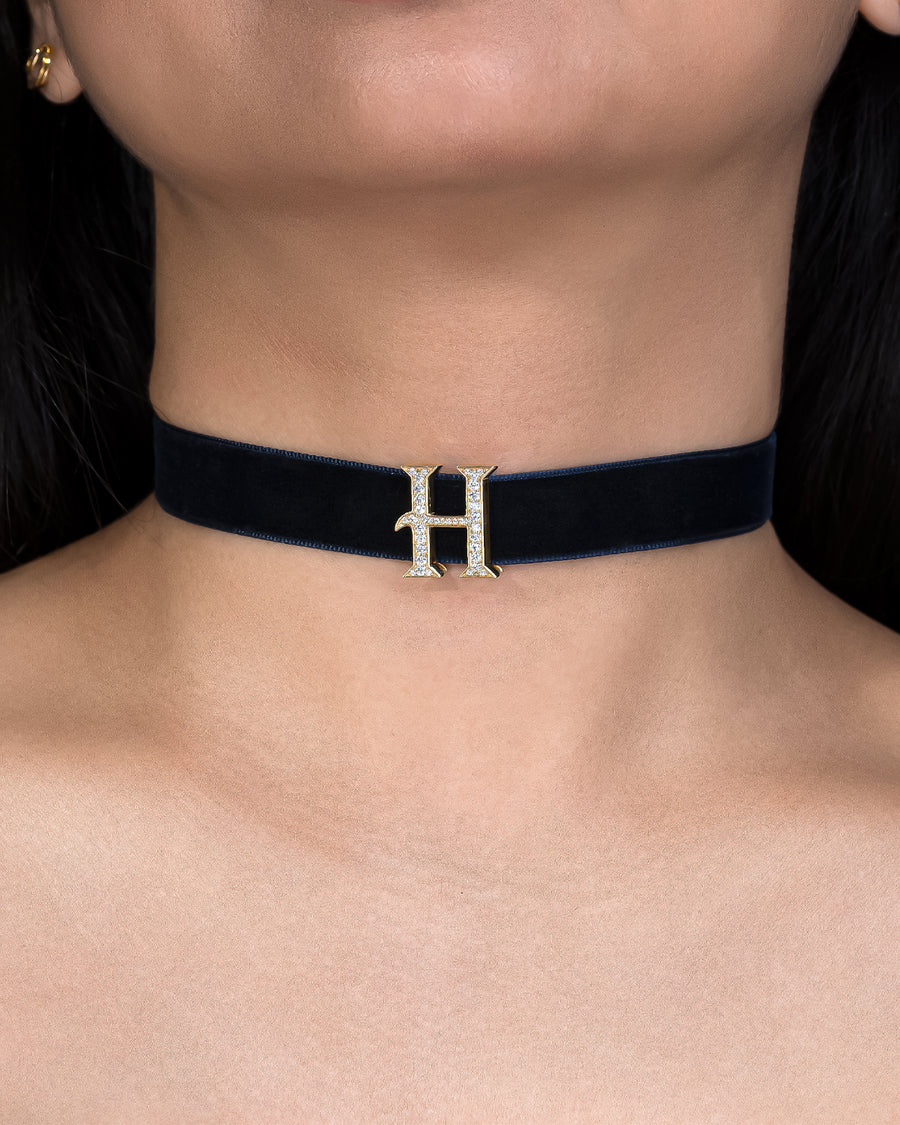 Navy blue choker with a gold 'H' pendant on a person's neck.
