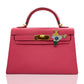 A pink handbag with a brooch featuring a floral design and the India flag colors attached to the clasp, collection-preview.