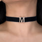 Black choker with a gold 'M' pendant on a person's neck