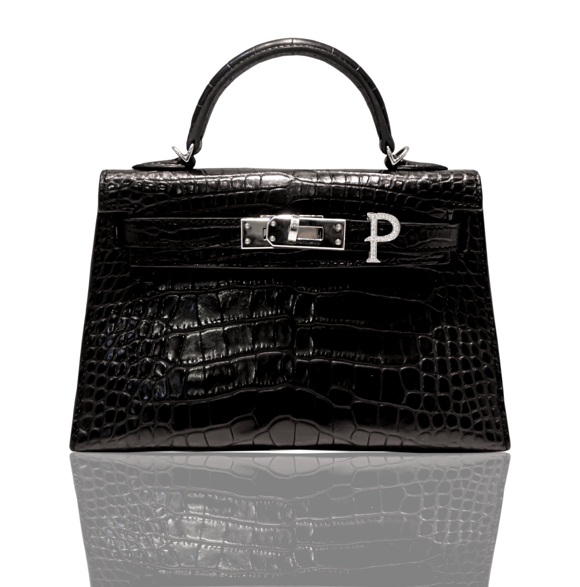 A black handbag with a crocodile pattern and a silver initial 'P' brooch attached to it, collection-preview.