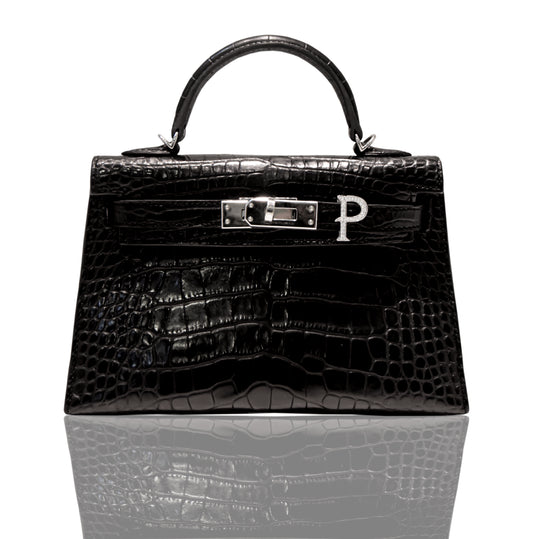 A black handbag with a crocodile pattern and a silver initial 'P' brooch attached to it, collection-preview.