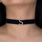 Black choker with a gold 'S' on a person's neck