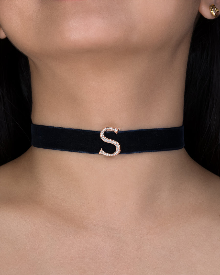 Black choker with a gold 'S' on a person's neck