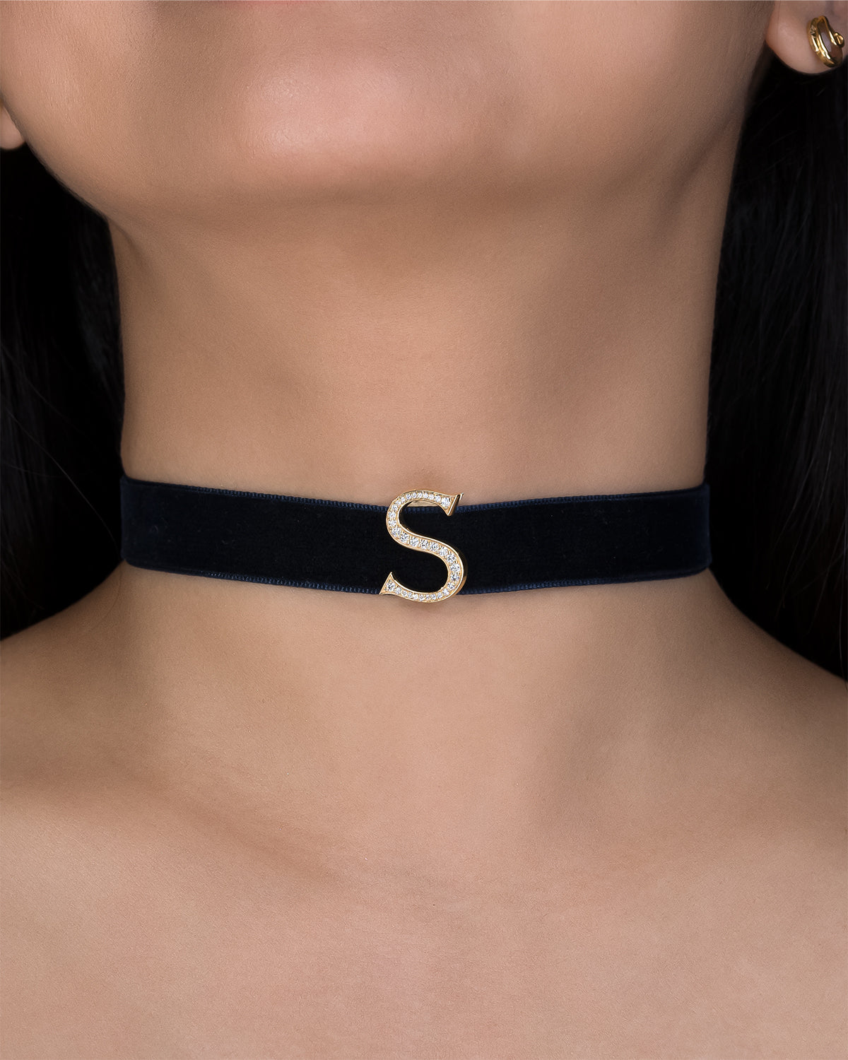 Navy blue choker with a gold 'S' on a person's neck