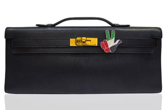 A black handbag with a metallic clasp and a decorative pin featuring geometric shapes and the colors red, green, and white. collection-preview.