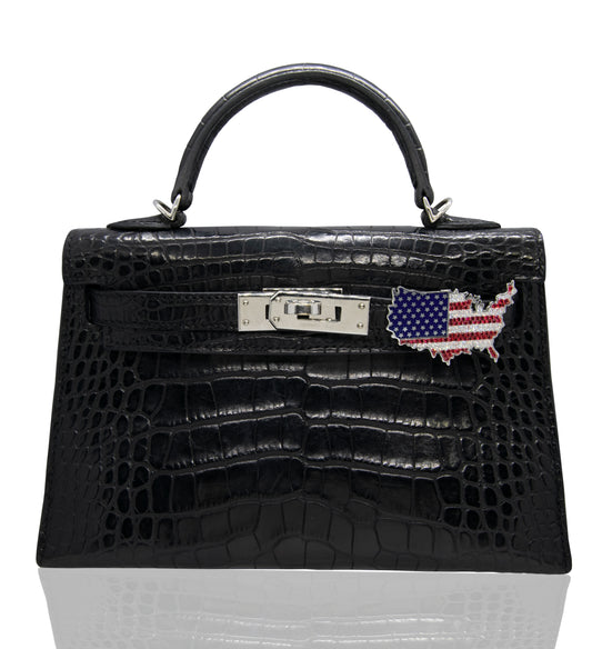 A black crocodile pattern handbag with a USA flag accessory attached to it, collection-preview.
