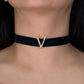 Black choker with a gold 'V' pendant on a person's neck against a dark background