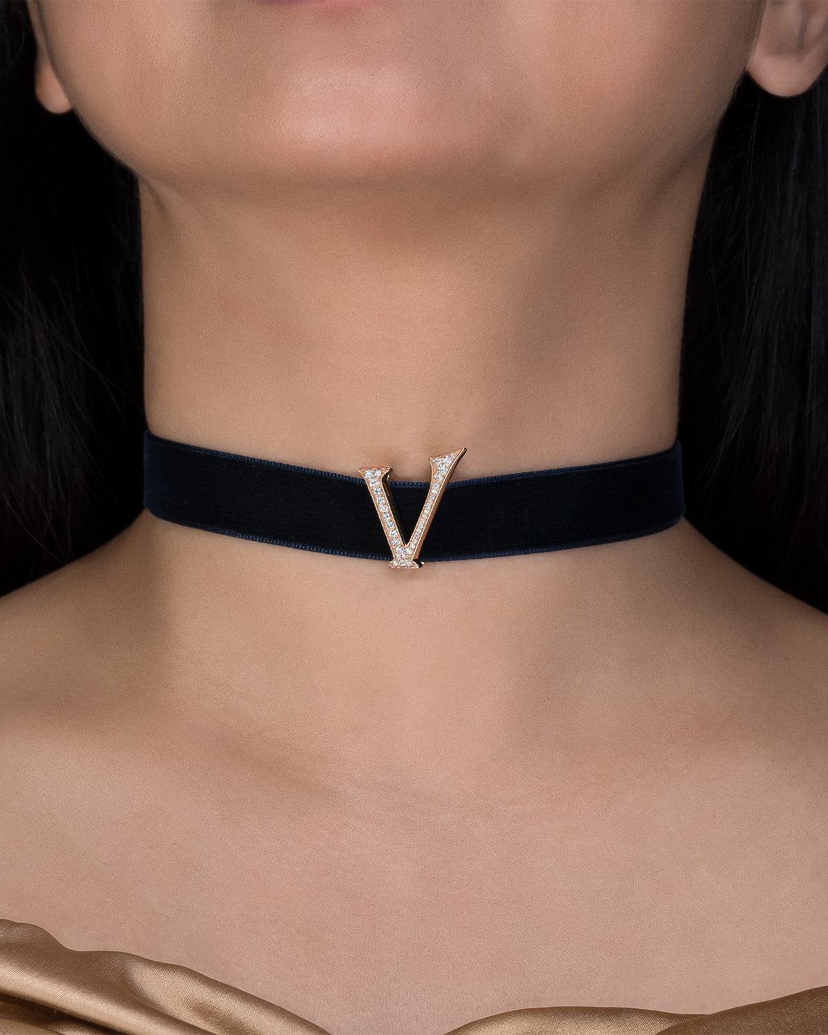 Black choker with a gold 'V' pendant on a person's neck against a dark background