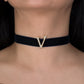 Black choker with a gold 'V' pendant on a person's neck against a dark background