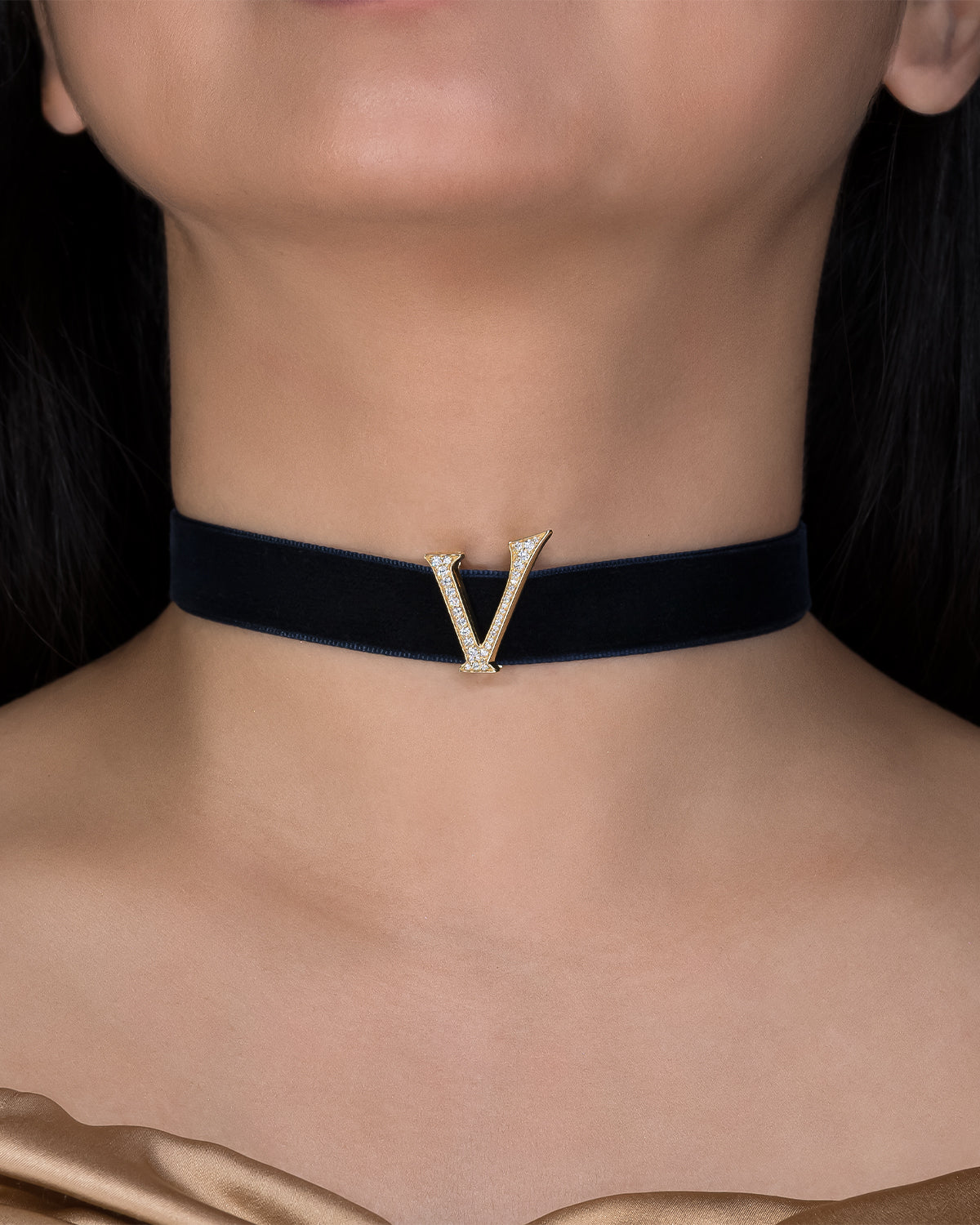 Black choker with a gold 'V' pendant on a person's neck against a dark background