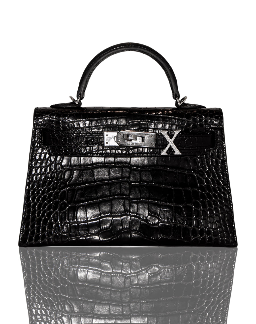 A black handbag with a crocodile pattern and a diamond-encrusted 'X' letter on the front, collection-preview.