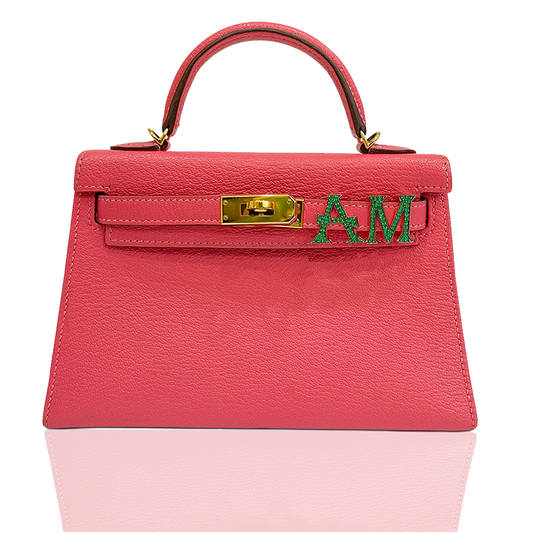 Pink handbag with gold clasp and green letters on a white background, collection-preview